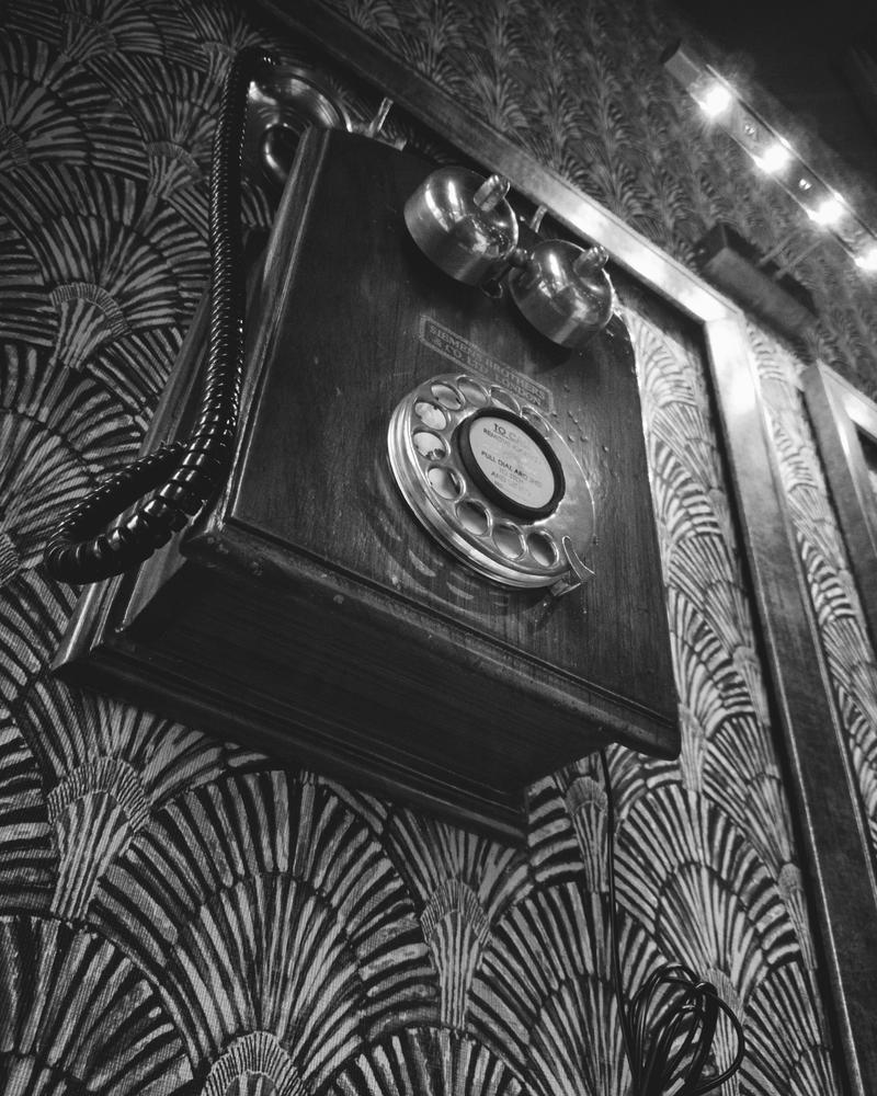 Old wall telephone with a rotary dial against patterned wallpaper